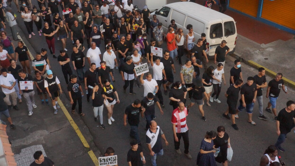 Un homme en t-shirt, au milieu de la foule habillée en noir, tient une pancarte sur laquelle est écrit : « STOP VIOLENCE » | © Mo News